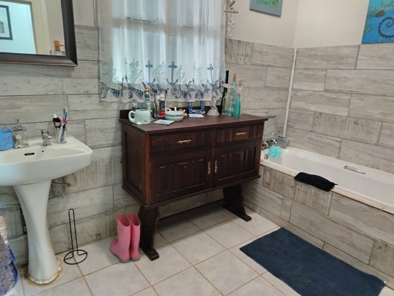 A bathroom featuring tiled wall cladding, a pedestal sink, and a built-in bathtub with neutral floor tiles.