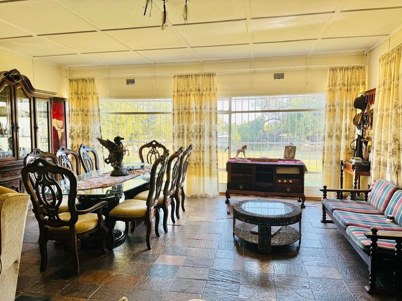 Spacious living and dining area featuring large windows with security bars, tiled flooring, and a classic panelled ceiling.