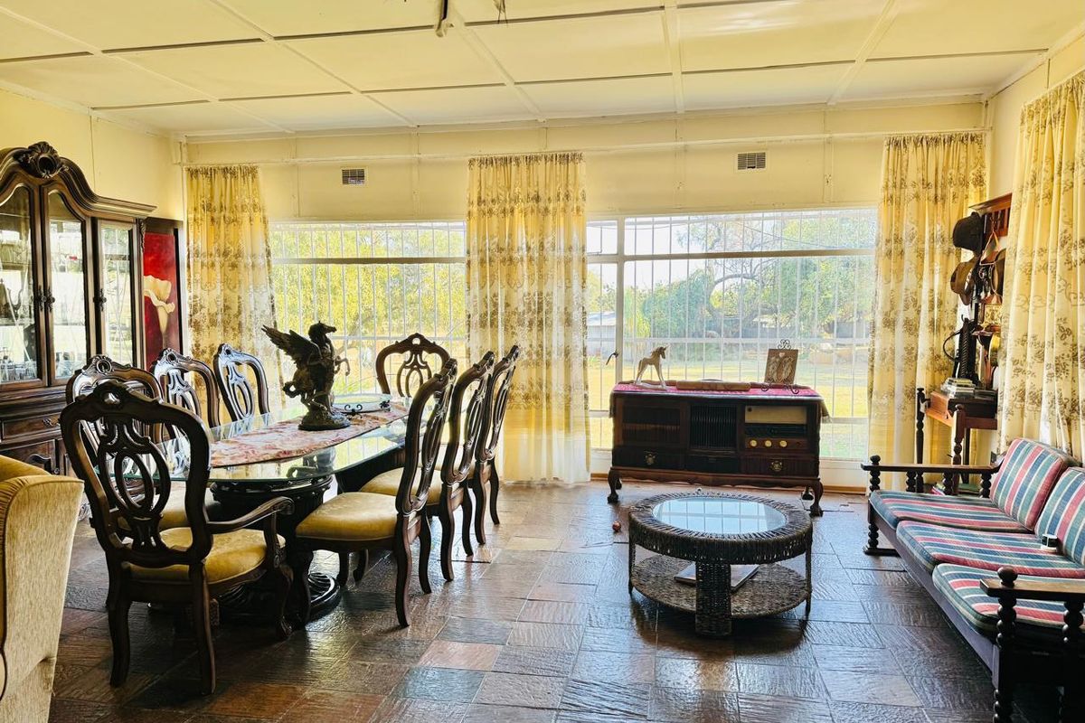 Spacious living and dining area featuring large windows with security bars, tiled flooring, and a classic panelled ceiling.