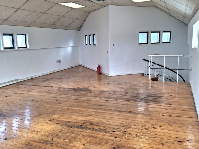 An open-plan office space featuring hardwood flooring, a suspended ceiling with recessed lighting, and a staircase with a safety railing.