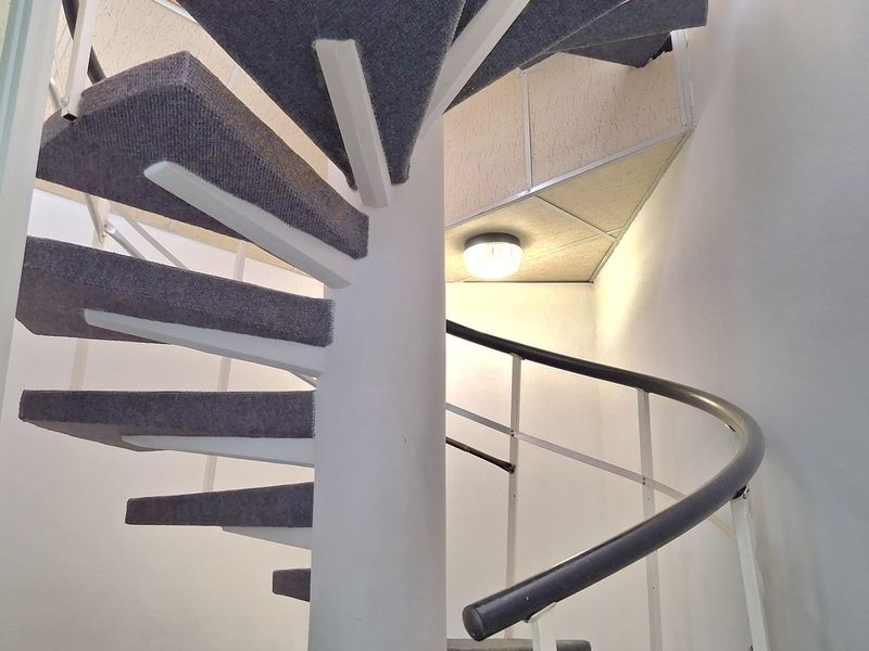 A functional spiral staircase with carpeted treads and a metal handrail, providing vertical access within the office space.