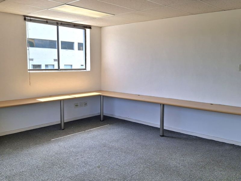 An empty office space featuring built-in desk surfaces, carpeted flooring, and a suspended ceiling with recessed lighting.