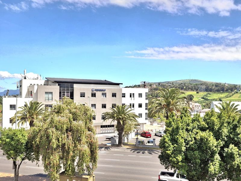 An elevated view overlooking a commercial office building, surrounding trees, and a public road.