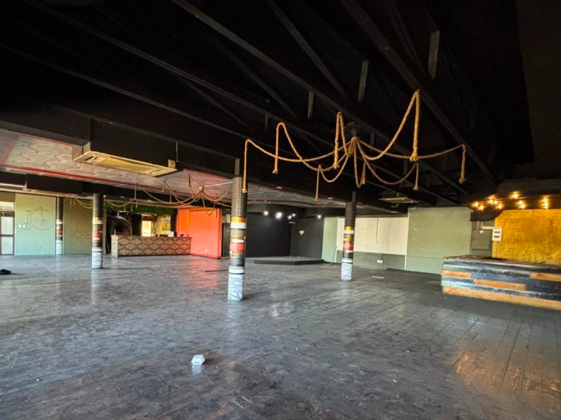 Spacious open-plan restaurant interior featuring exposed ceiling trusses, support columns, and a built-in bar area, offering a versatile layout for dining or events.