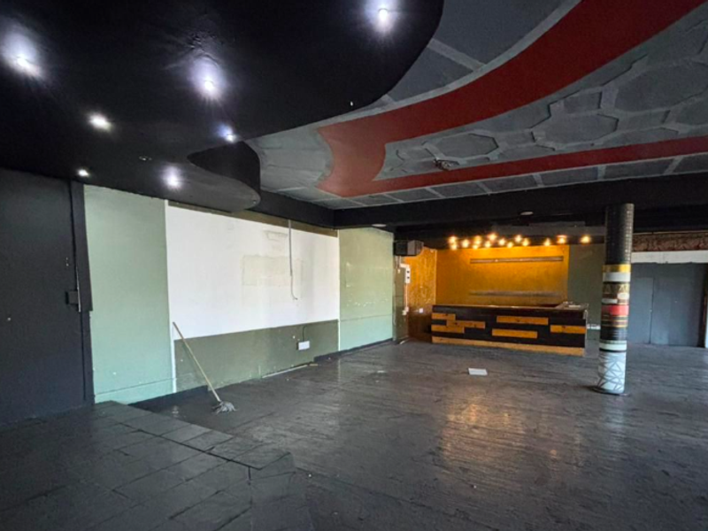 Spacious open-plan restaurant interior featuring a built-in service counter, decorative ceiling bulkheads, and recessed lighting, currently in need of cosmetic refurbishment.
