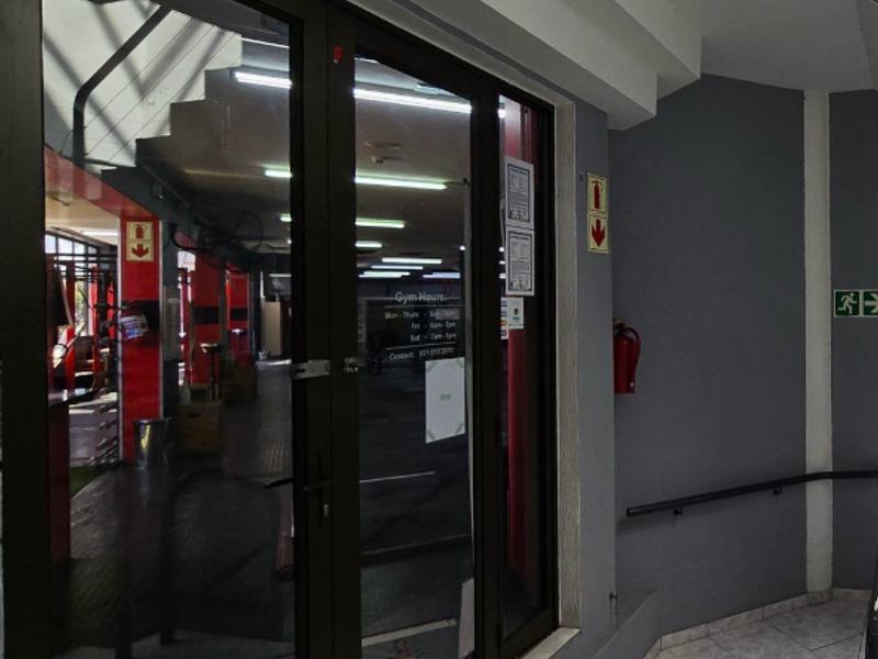 Entrance area featuring glass double doors, tiled flooring, and safety fixtures including a handrail and fire extinguisher.