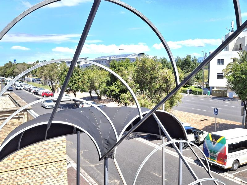 An elevated street-level view featuring a decorative metal arch structure and fabric awning overlooking a public road and surrounding urban landscape.