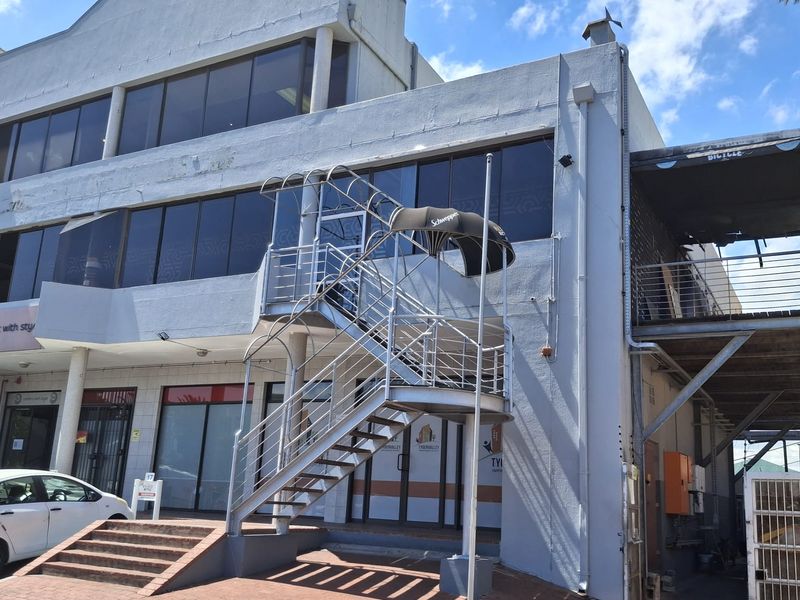 Exterior view of a multi-story commercial building featuring a prominent metal staircase, glass facade, and paved entrance area.