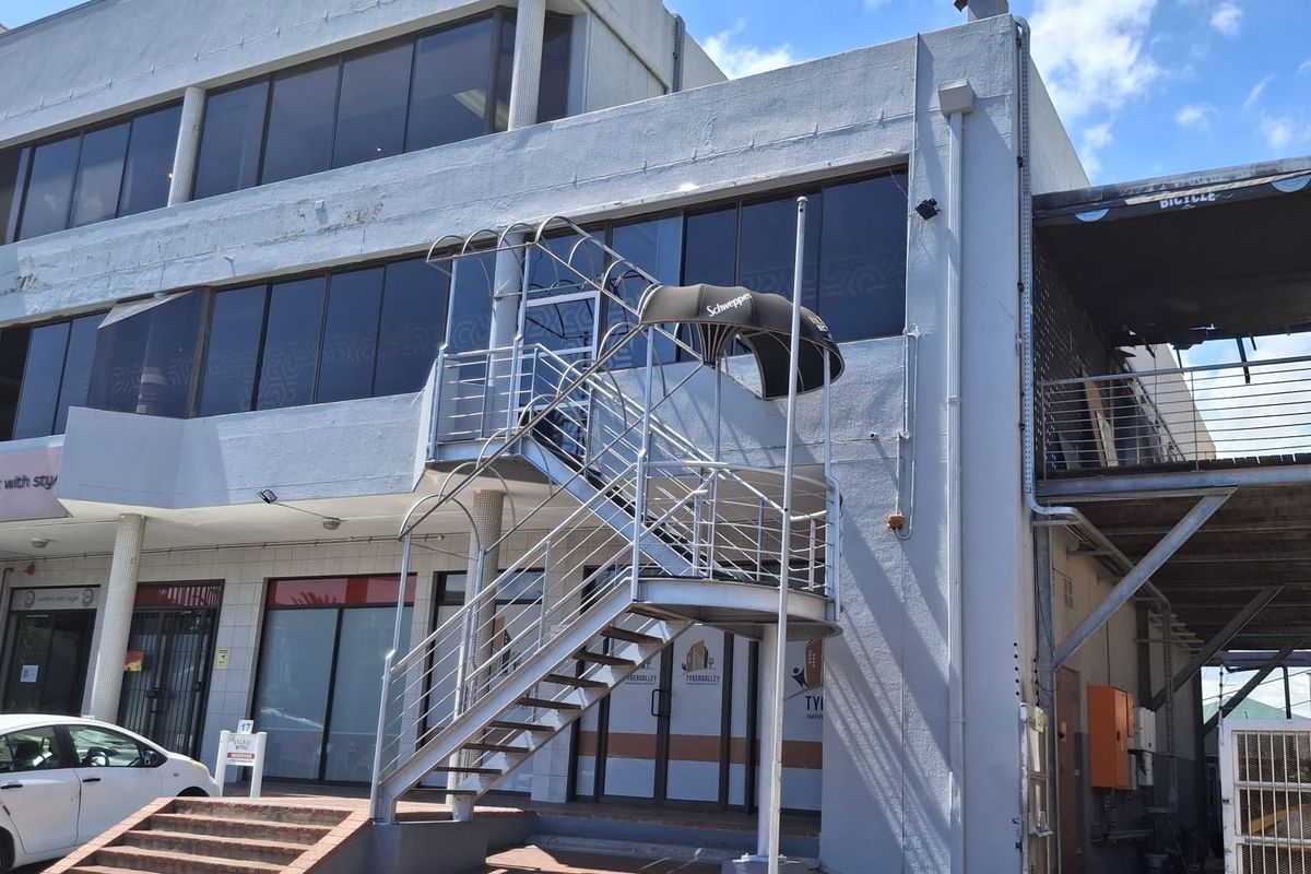 Exterior view of a multi-story commercial building featuring a prominent metal staircase, glass facade, and paved entrance area.