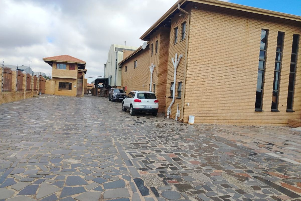 Exterior view of the industrial property featuring a paved courtyard, brick facade, and secure perimeter fencing.