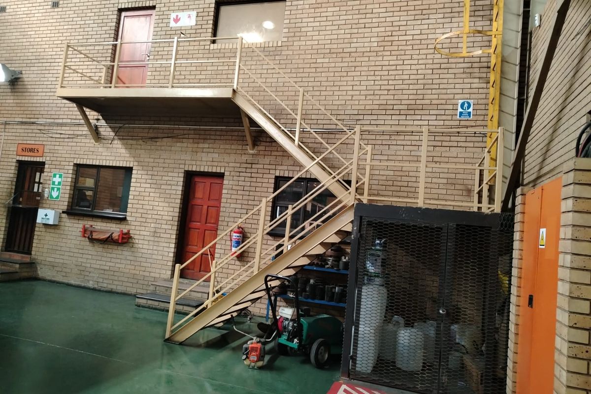 Industrial courtyard area featuring a metal staircase, brick facade, and secure storage enclosure with epoxy-coated flooring.