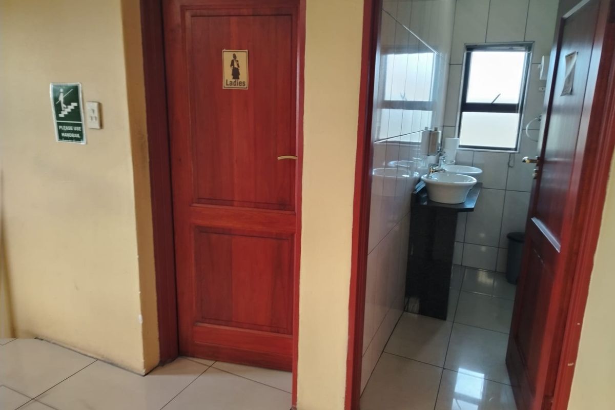 A functional ladies' restroom facility featuring tiled flooring, wall-mounted basins, and a solid timber door entrance.