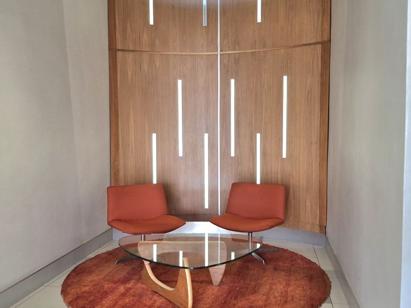 A modern office reception or breakout area featuring a curved wood-paneled feature wall with integrated vertical LED lighting and polished tile flooring.