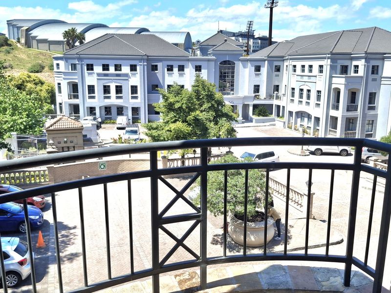 Elevated balcony with metal balustrade overlooking a paved office complex courtyard and parking area.