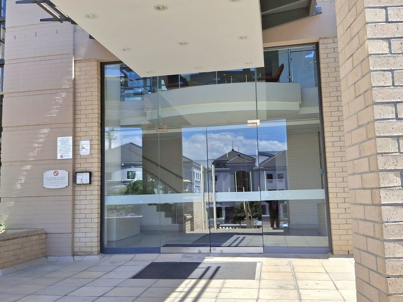 Modern office building entrance featuring a glass double door entry, tiled patio area, and a protective overhead canopy.