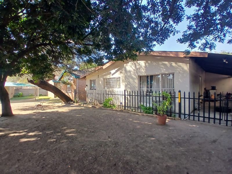 Rear view of the office property featuring a covered patio area, metal security fencing, and established trees on the grounds.