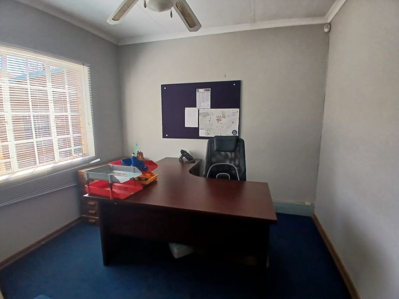A functional office space featuring carpeted flooring, a ceiling fan, and window blinds, providing a practical environment for professional use.
