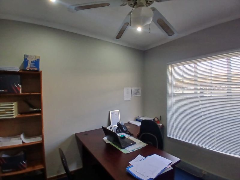 A functional office space featuring a ceiling fan, venetian blinds, and recessed lighting, providing a practical environment for professional work.