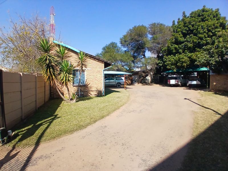 Exterior view of the office property featuring a brick facade, carport parking, and a large yard area with a precast boundary wall.