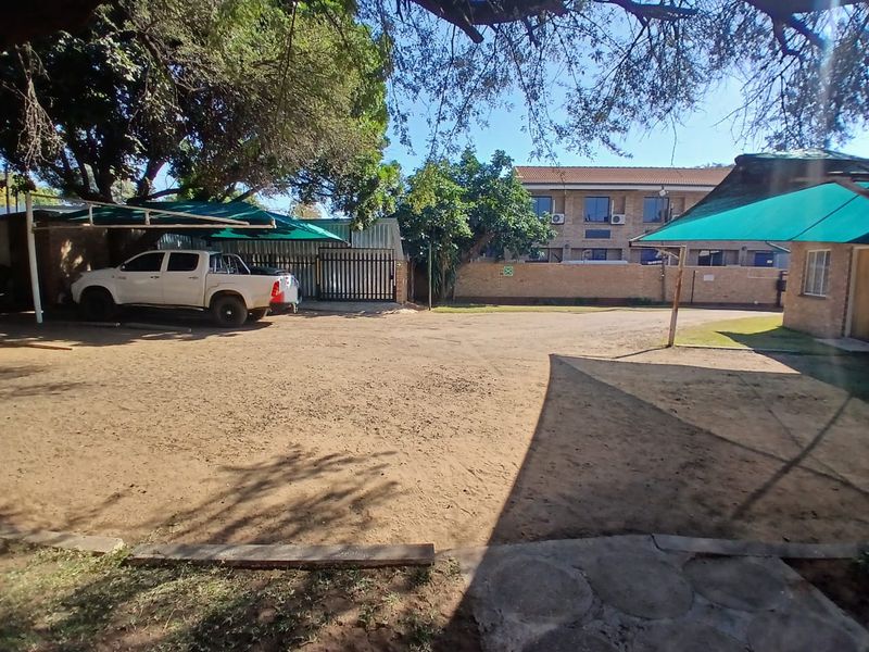 Exterior view of the office property featuring a large unpaved parking area, shade cloth carports, and secure perimeter walling.
