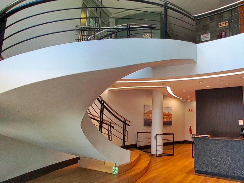 Modern office building entrance featuring a striking spiral staircase, reception desk, and high-quality finishes in a bright, professional lobby area.