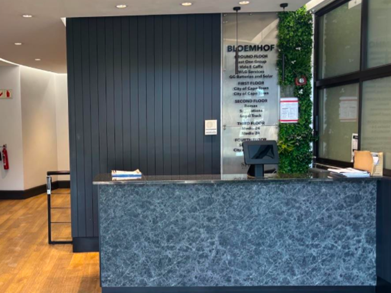 Modern office building reception area featuring a marble-finish desk, directory signage, timber flooring, and a decorative vertical garden wall.