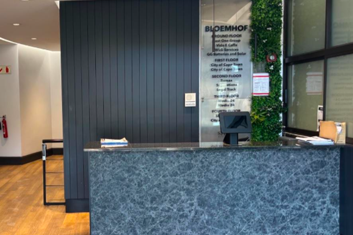 Modern office building reception area featuring a marble-finish desk, directory signage, timber flooring, and a decorative vertical garden wall.