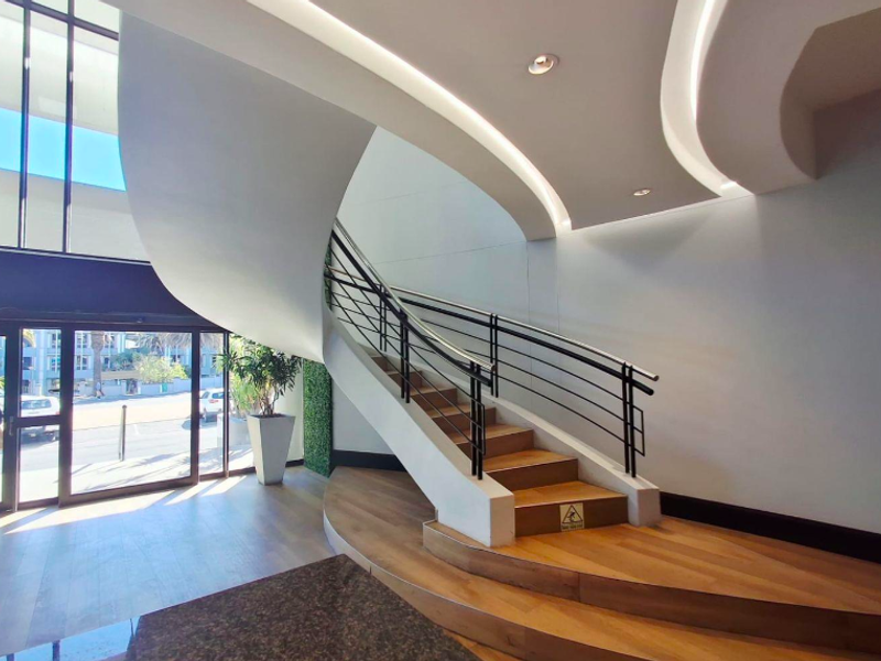 Modern office building entrance featuring a striking curved staircase, high ceilings with recessed lighting, and large glass doors providing ample natural light.