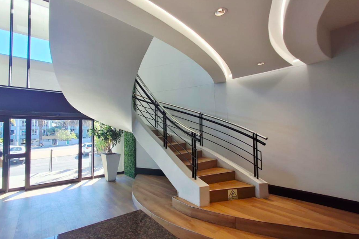 Modern office building entrance featuring a striking curved staircase, high ceilings with recessed lighting, and large glass doors providing ample natural light.