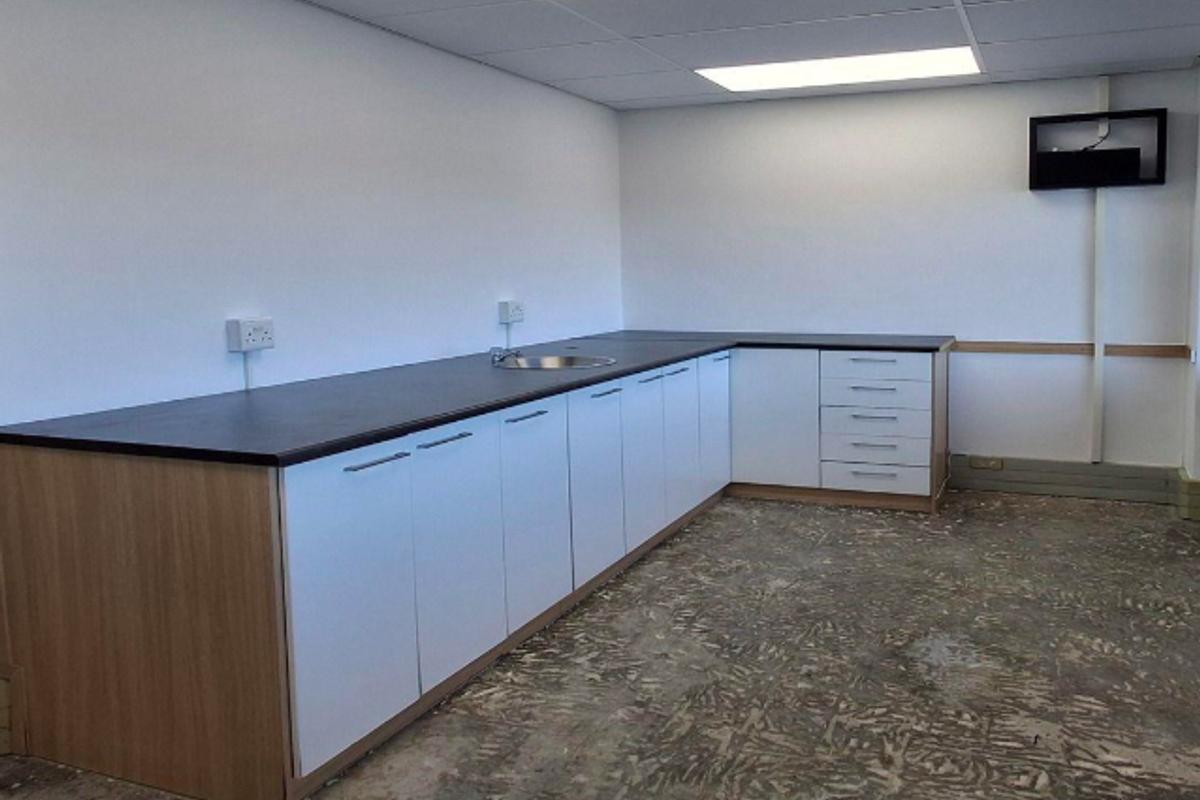 A functional office kitchenette featuring built-in cabinetry, laminate countertops, and a drop-in sink, currently awaiting final flooring installation.