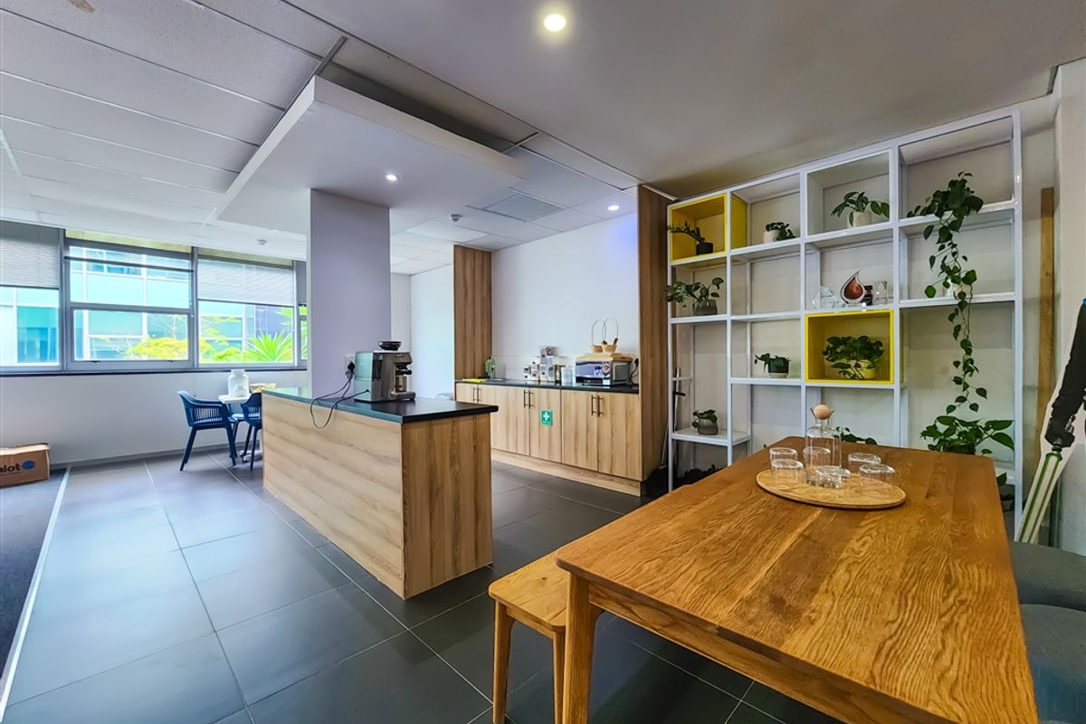 Modern office breakroom featuring a kitchenette with wood-finish cabinetry, dark tiled flooring, and integrated shelving, creating a functional and inviting communal workspace.