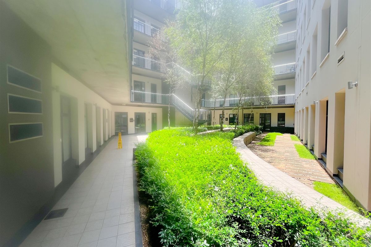A well-maintained central courtyard area within an office complex, featuring paved walkways, landscaped garden beds, and multi-level building access.