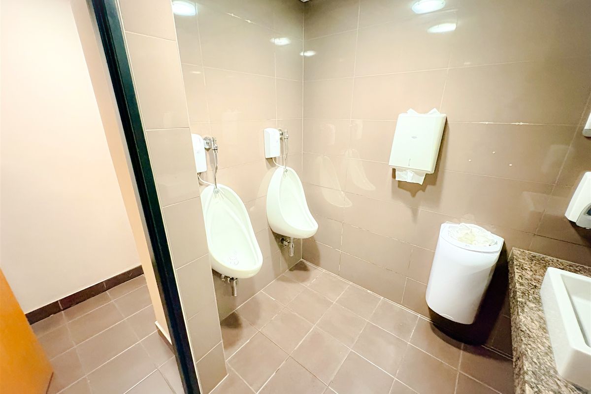 A functional office restroom featuring wall-mounted urinals, tiled walls and flooring, and a granite-topped vanity area.