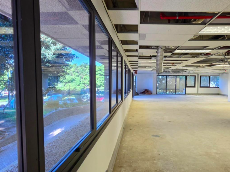 An expansive, vacant office space featuring large windows, exposed ceiling infrastructure, and a suspended grid system, ready for custom fit-out.