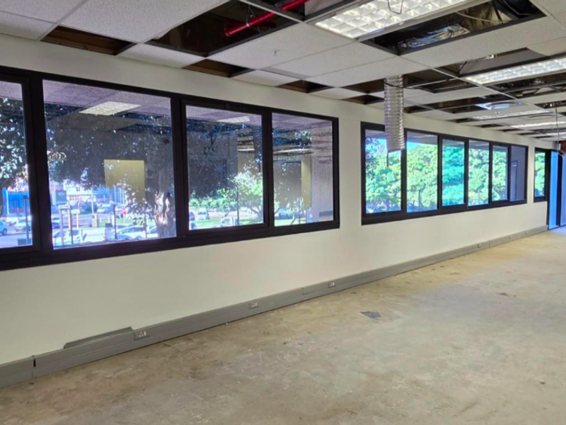 An expansive, open-plan office space featuring large windows, perimeter electrical trunking, and a partially unfinished suspended ceiling.