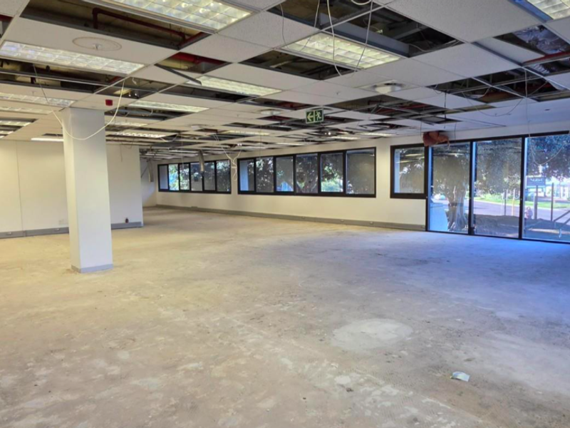Open-plan office space featuring large windows, a structural column, and a suspended ceiling grid currently undergoing maintenance with missing tiles.