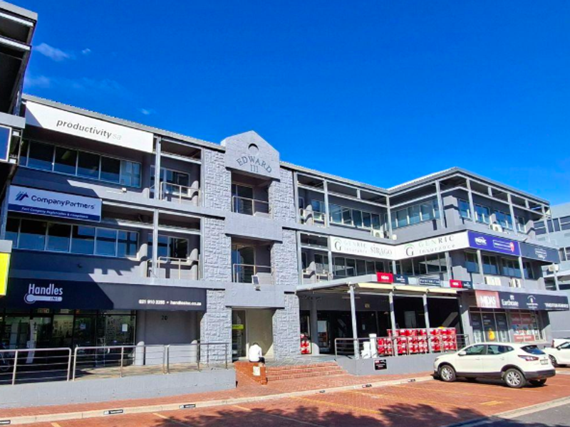 Front elevation of a multi-story commercial office building featuring stone masonry accents, glass windows, and ground-level retail signage with paved parking.