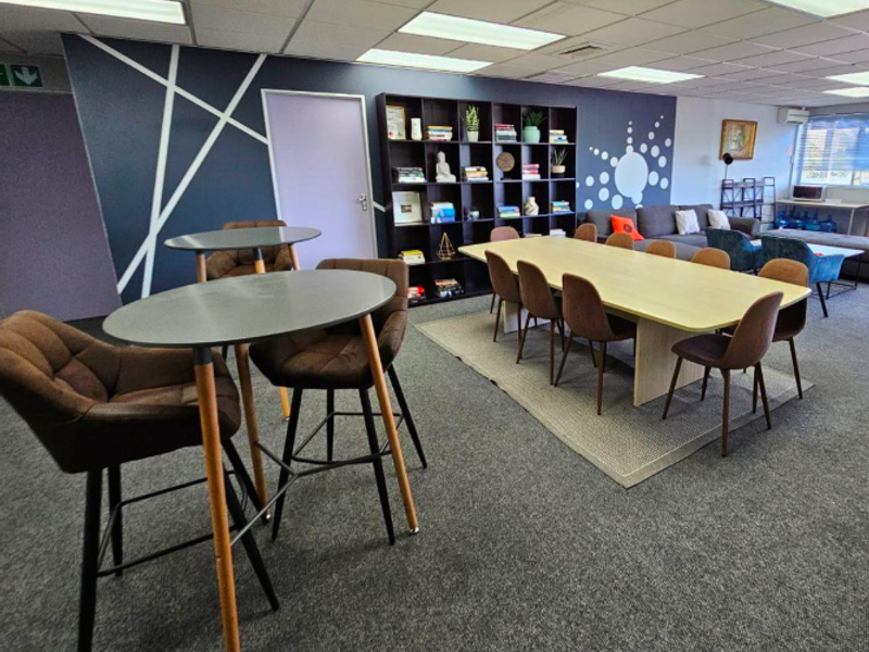 A spacious office area featuring a suspended ceiling, recessed lighting, carpeted flooring, and a large built-in shelving unit.