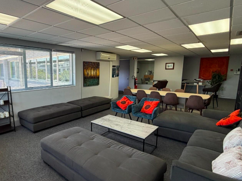 A spacious, well-lit office area featuring a suspended ceiling, recessed lighting, air conditioning, and large windows with venetian blinds.