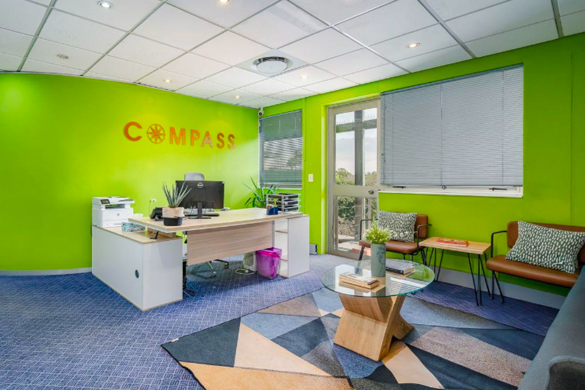 A bright office space featuring a suspended ceiling with recessed lighting, carpeted flooring, and an aluminium-framed glass door with venetian blinds.