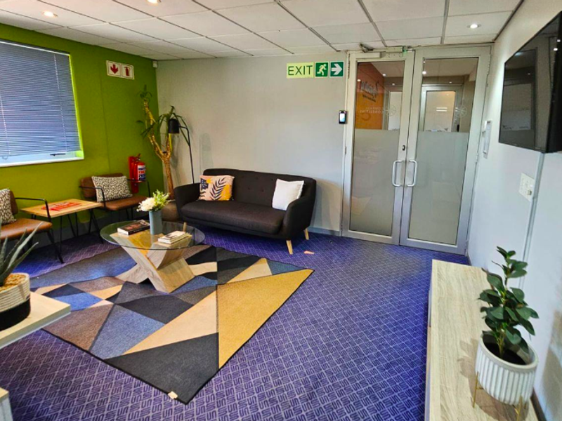 A functional office reception area featuring a suspended ceiling, recessed lighting, and secure aluminium-framed glass entry doors.