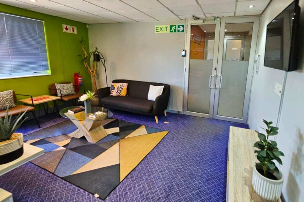 A functional office reception area featuring a suspended ceiling, recessed lighting, and secure aluminium-framed glass entry doors.