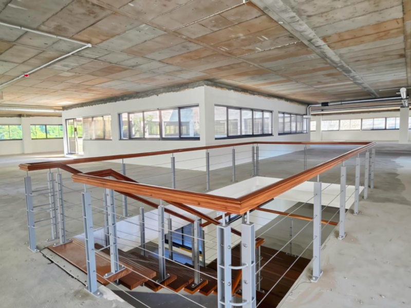 Spacious open-plan office area featuring an exposed concrete ceiling, timber staircase with modern balustrade, and large windows providing ample natural light.