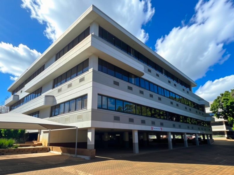 A modern multi-story office building featuring a clean facade, tinted windows, and a convenient ground-level undercover parking area with paved driveway access.