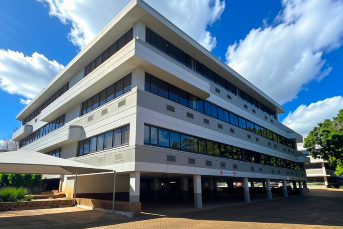 A modern multi-story office building featuring a clean facade, tinted windows, and a convenient ground-level undercover parking area with paved driveway access.