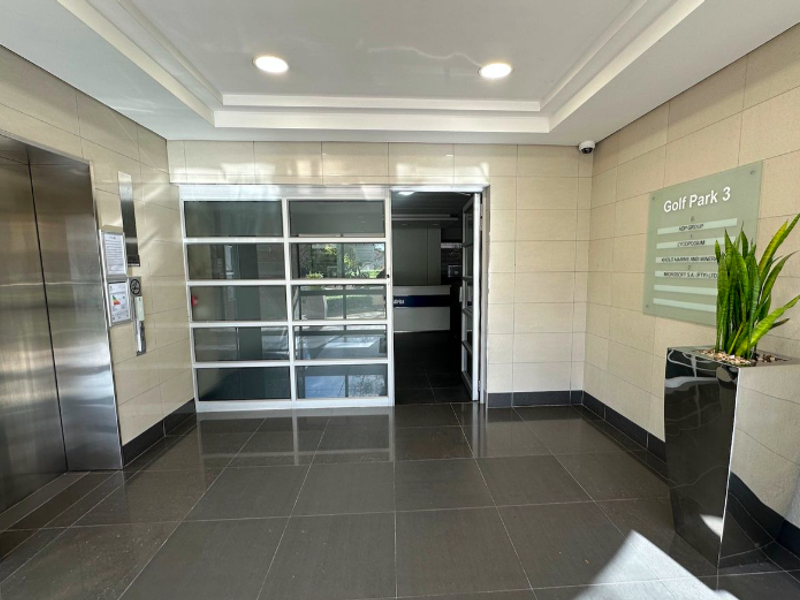 Modern office building lobby featuring a stainless steel elevator, tiled flooring, recessed lighting, and a clear tenant directory signage.