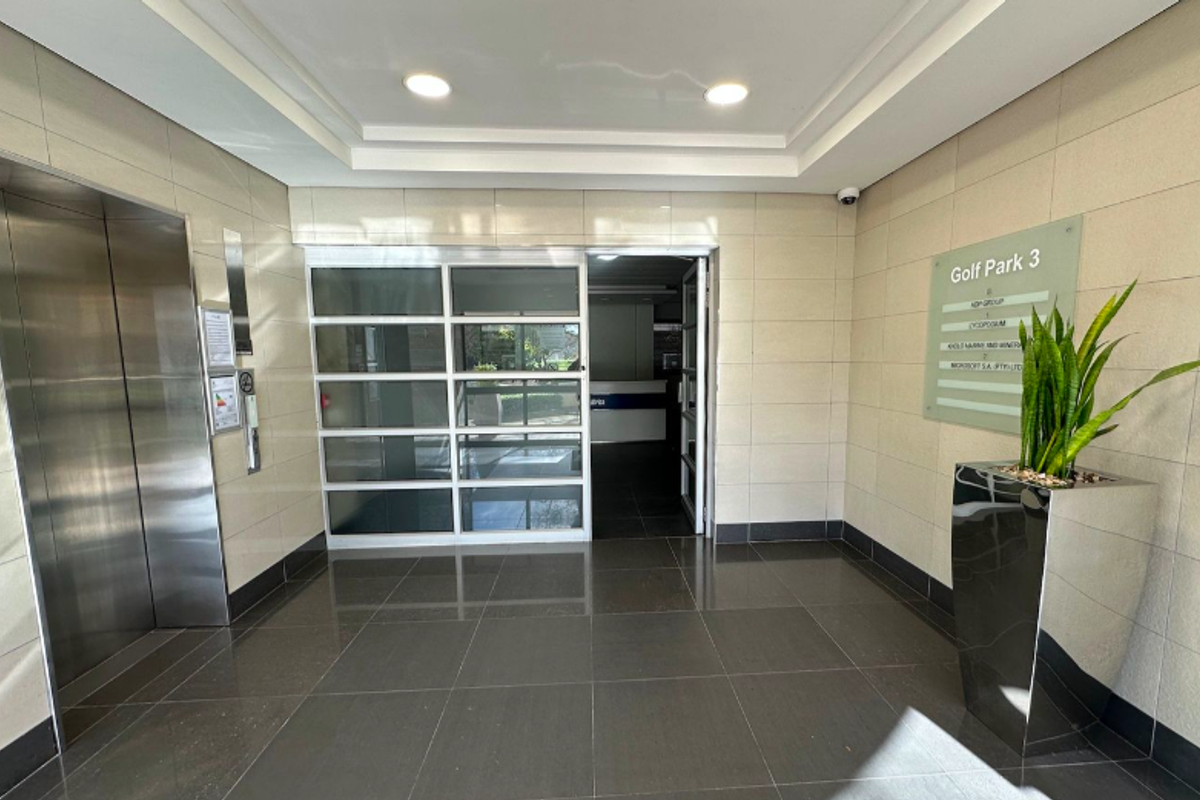Modern office building lobby featuring a stainless steel elevator, tiled flooring, recessed lighting, and a clear tenant directory signage.