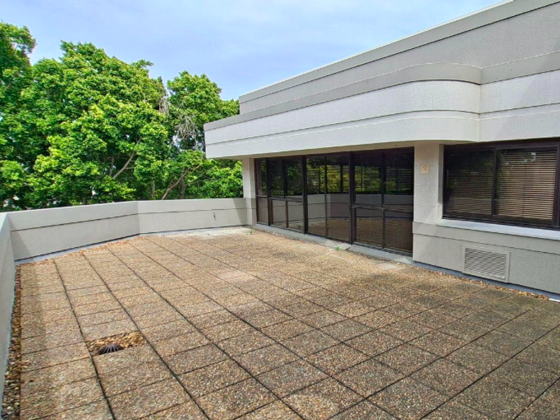 A spacious outdoor terrace featuring paved flooring, a protective parapet wall, and large sliding glass doors providing access to the office interior.
