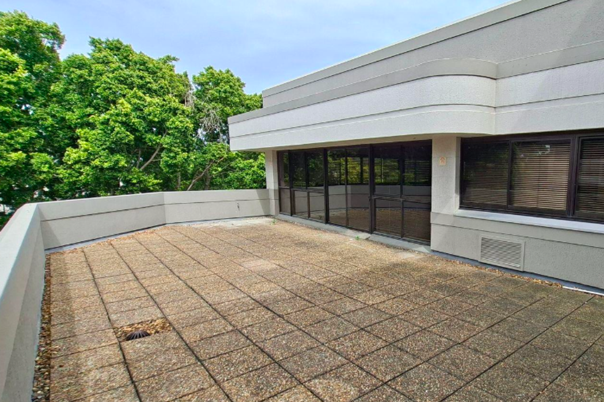 A spacious outdoor terrace featuring paved flooring, a protective parapet wall, and large sliding glass doors providing access to the office interior.