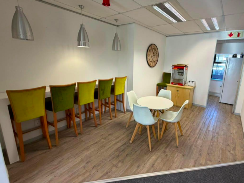 A modern office breakroom area featuring laminate flooring, a suspended ceiling with recessed lighting, and a built-in breakfast bar counter.
